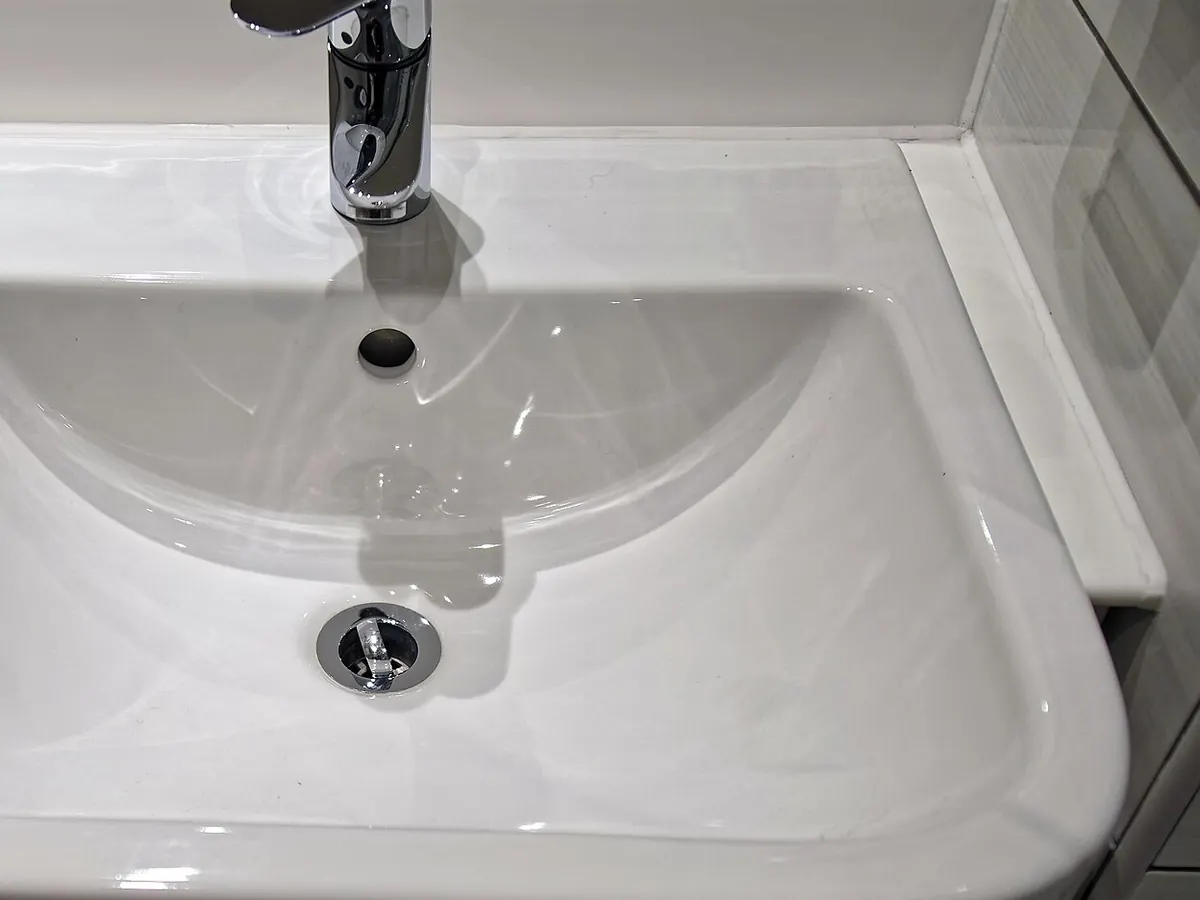 A chrome single-lever faucet over a white ceramic basin with a round chrome drain